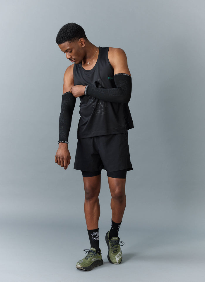A model adjusts the black PCVL Arm Compression sleeve from Percival, styled with a full black athletic training kit.