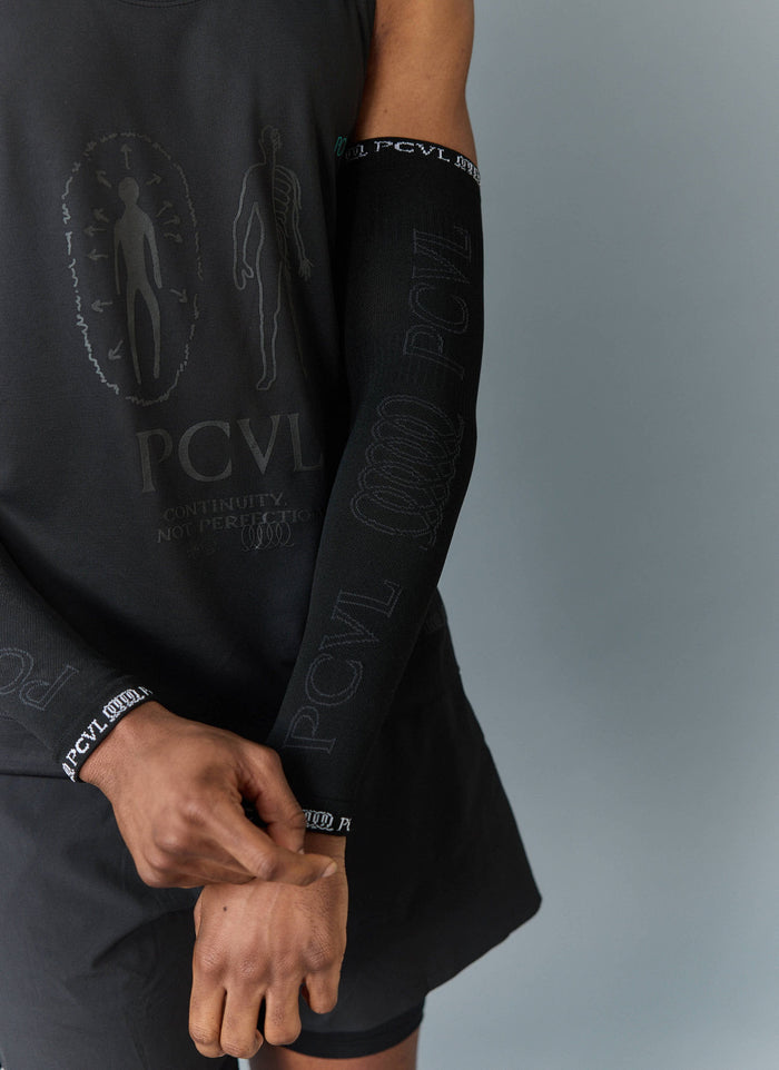 Close up of a model wearing the Percival PCVL Arm Compression sleeve in black, showing the jacquard logo detailing.