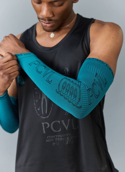Close up of a model wearing the blue PCVL Arm Compression sleeves from Percival, showing the jacquard logo.