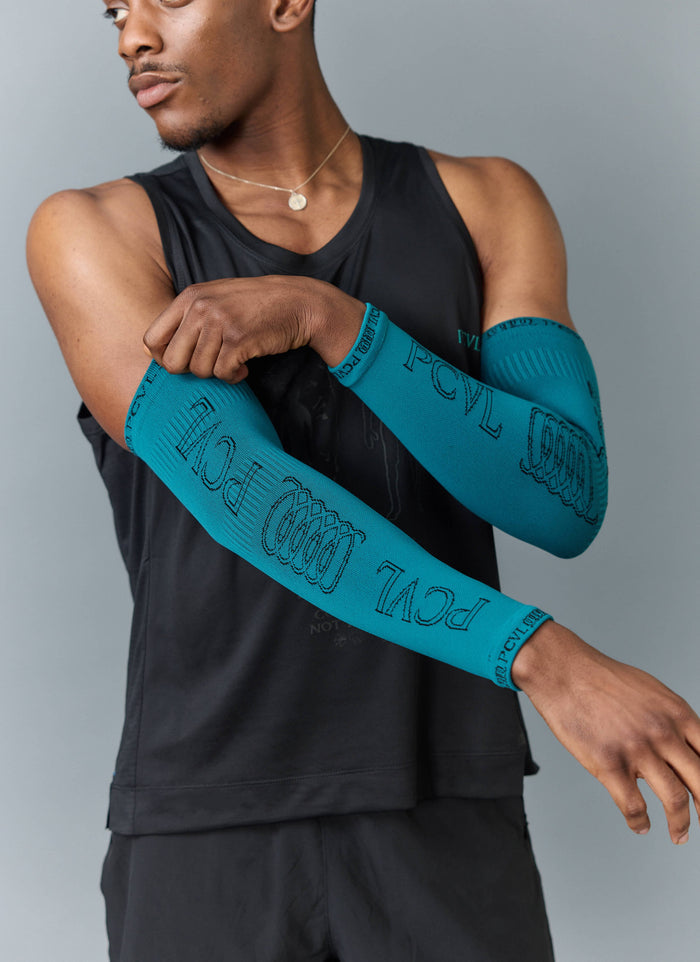 A model wears the Percival PCVL Arm Compression sleeves in blue, showing the detailed jacquard knit logo and pattern.