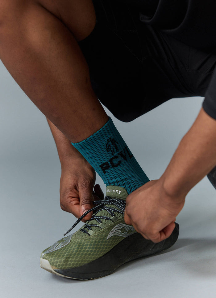 A close-up of a model wearing the blue ribbed PCVL Sport Socks from Percival while tying the laces of their trainers.