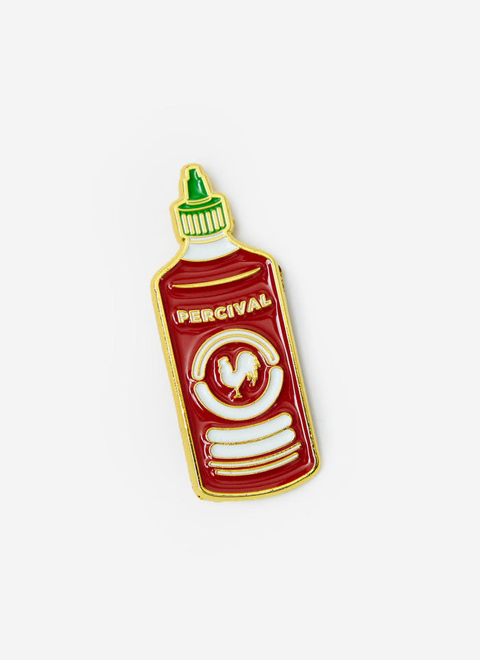 The Percival Hot Sauce Pin Badge, a red and gold enamel pin designed to look like a sriracha bottle, on a white background.