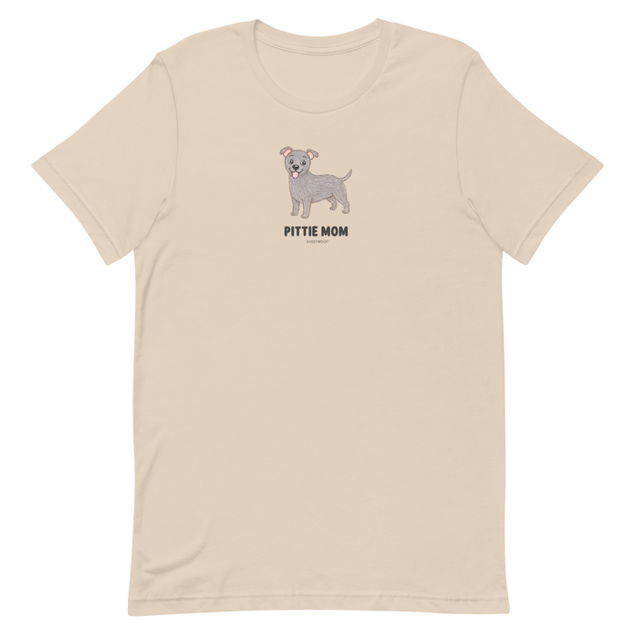 The Pittie Mom Tee by Sassy Woof is a light beige unisex shirt with a cartoon grey pitbull and "PITTIE MOM" text—perfect for pitbull lovers to show off their pup pride.