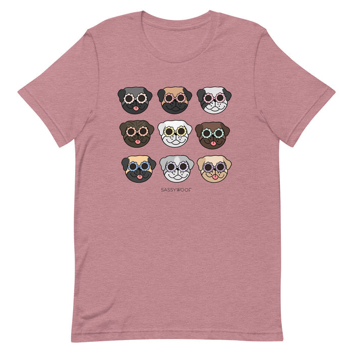 The Pug Tee by Sassy Woof is a mauve unisex shirt with nine cartoon pug faces in colorful glasses and expressions, plus “SASSY WOOF” printed below. A fun choice for any dog lover!.