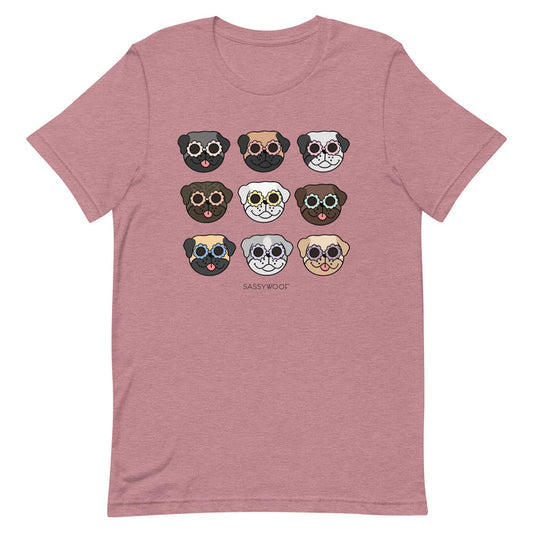 The Pug Tee by Sassy Woof is a mauve unisex shirt with nine cartoon pug faces in colorful glasses and expressions, plus “SASSY WOOF” printed below. A fun choice for any dog lover!.