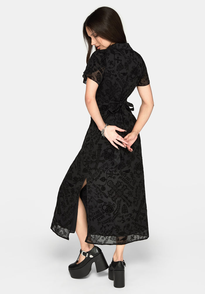 A woman modeling a black short-sleeve midi dress with a lace overlay and a tie waist, shown from a three-quarters back angle against a light gray studio background.