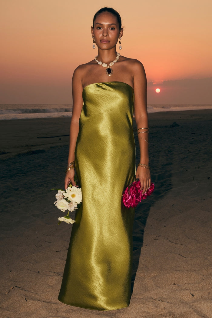 Chartreuse satin strapless maxi dress styled on the beach at sunset with pink clutch.
