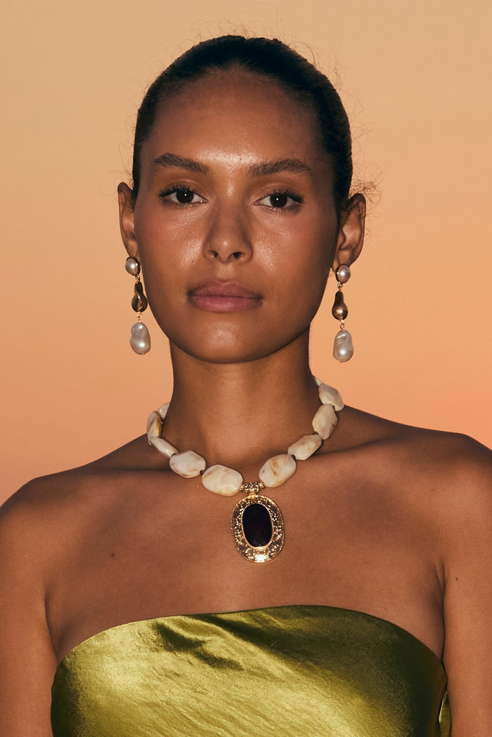 Model in green satin top wearing a beaded stone statement pendant necklace and pearl earrings.