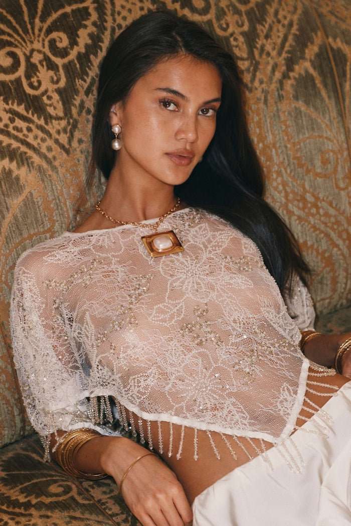 Woman wearing an ivory fringe shawl top with sheer floral lace and a square pendant necklace