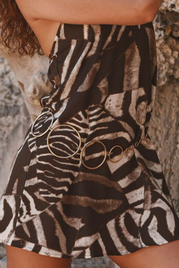 Gold circle-link chain belt worn over a zebra-print resort dress.