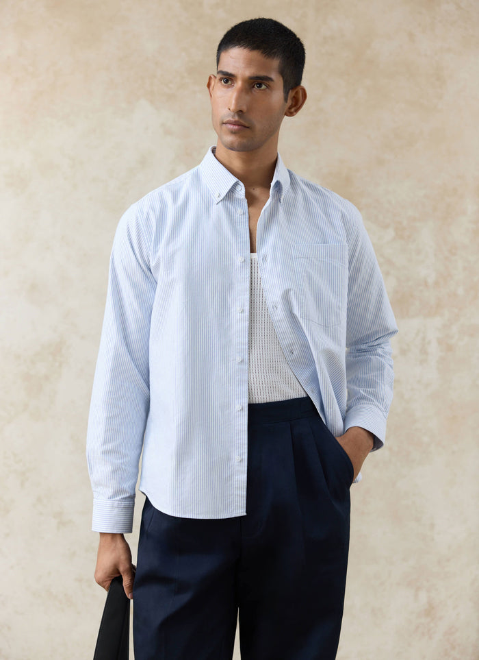 Percival blue striped cotton Oxford shirt with a button-down collar, worn open over a white vest and navy trousers.