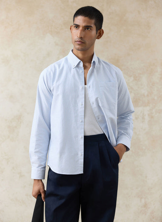 Percival blue striped cotton Oxford shirt with a button-down collar, worn open over a white vest and navy trousers.