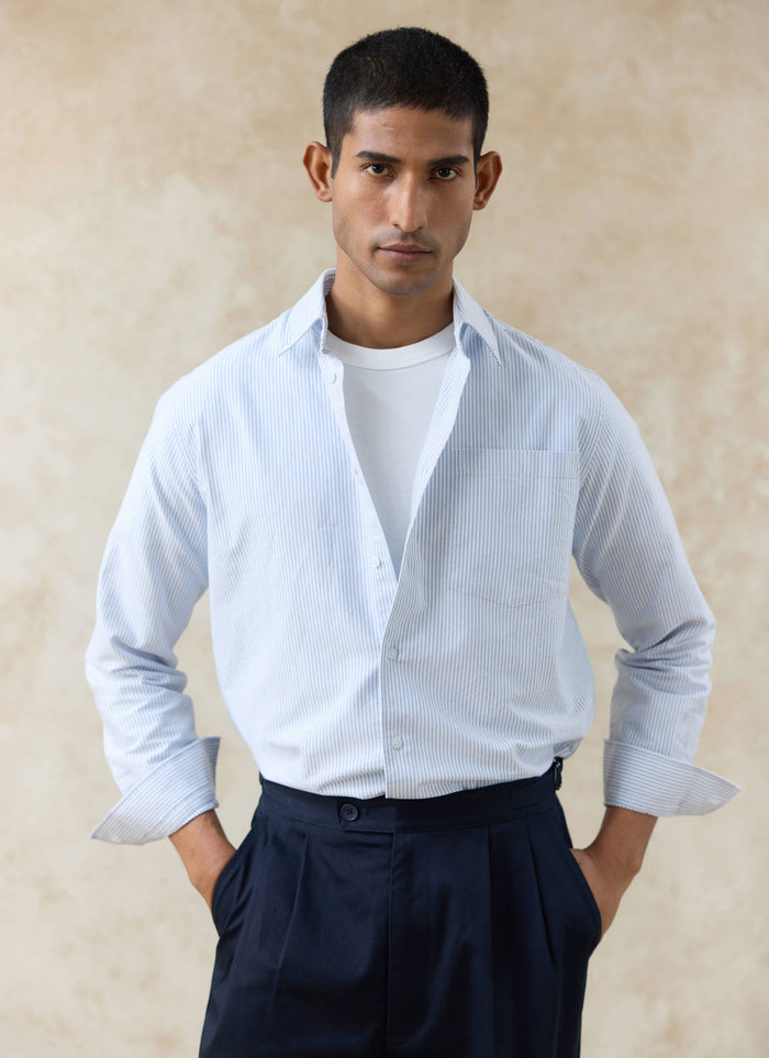 Percival blue striped cotton Oxford shirt styled open over a white t-shirt with navy pleated trousers.