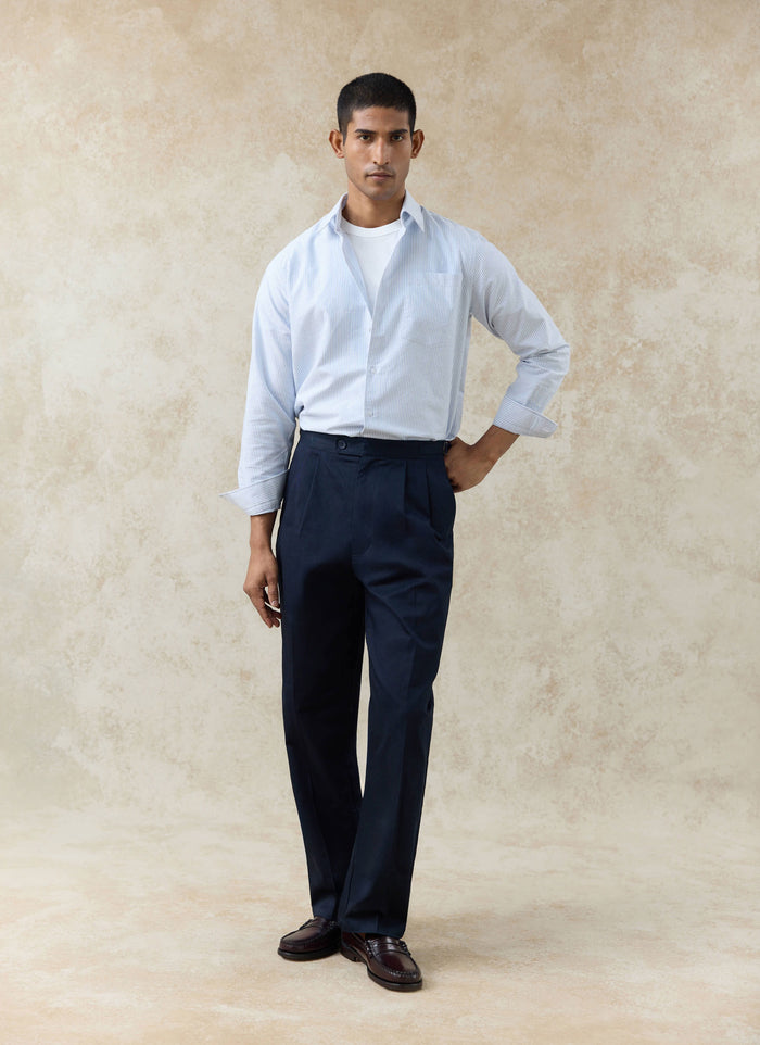 Percival blue striped Oxford shirt and navy cotton double pleated Blake trousers styled against a textured beige wall.