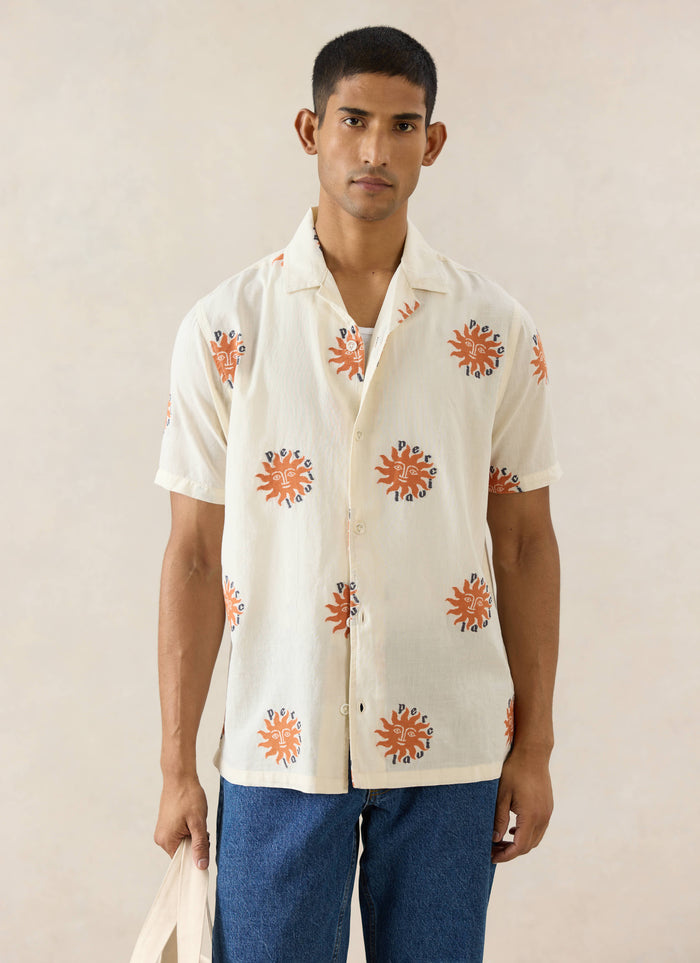 The Percival Sun Cuban Shirt in cream cotton with orange sun embroidery, styled on a model with blue jeans.