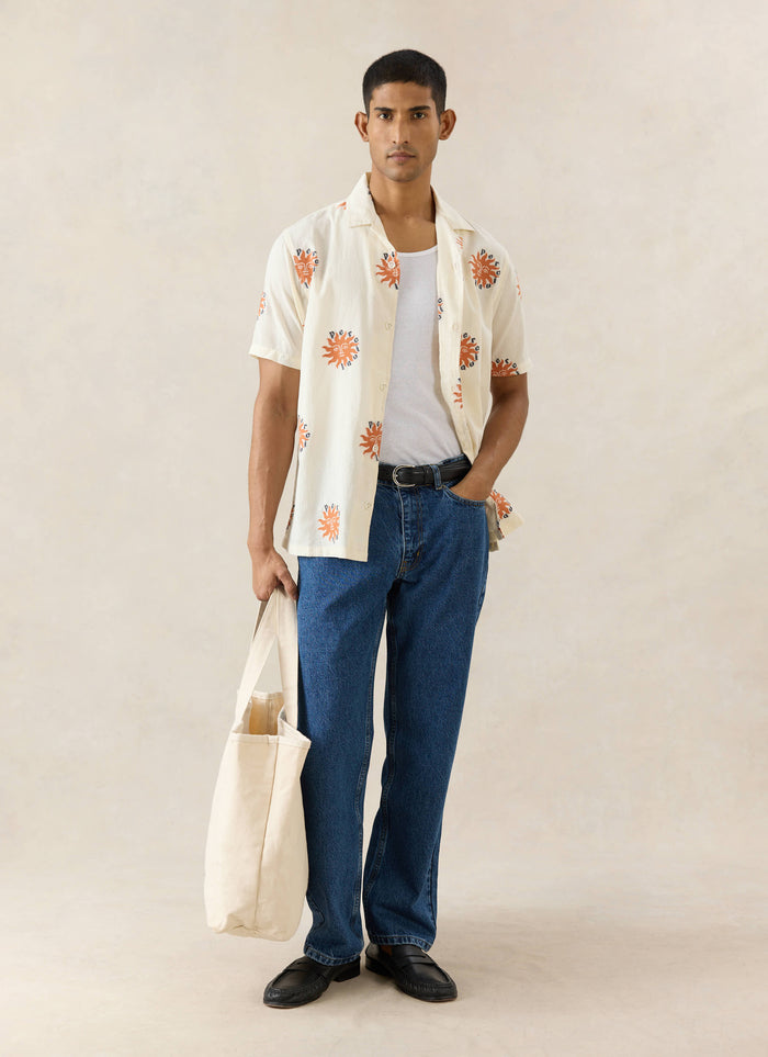 The Percival Sun Cuban Shirt in cream cotton with orange embroidery, styled with blue jeans and a cream tote bag.