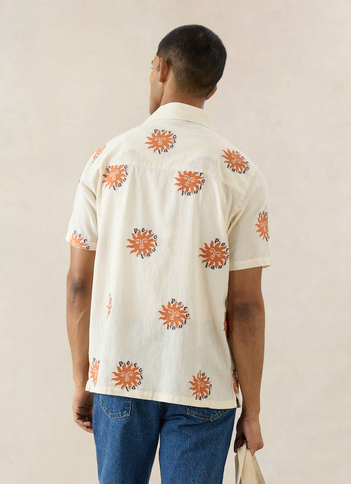 The Percival Sun Cuban Shirt in cream cotton with orange embroidered suns, shown from behind on a model in blue jeans.