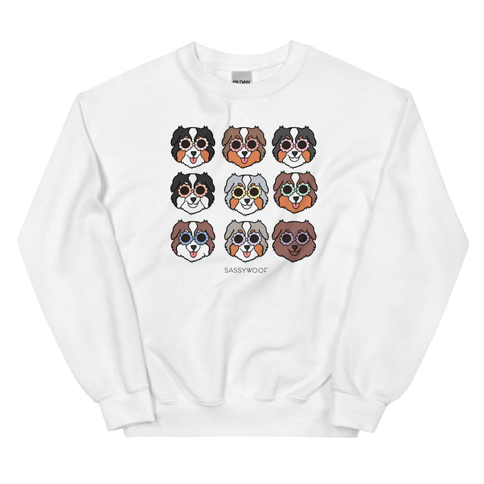 The "Sweatshirt - Aussies" by Sassy Woof is a white unisex crewneck featuring nine illustrated dog faces with different fur patterns and round glasses. "SASSYWOOL" is printed below the design. Comfortable for any occasion.