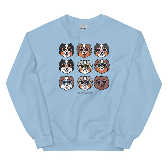 The Sweatshirt - Aussies by Sassy Woof is a light blue unisex crewneck with nine cartoon Aussie dog faces in sunglasses and Sassy Woof printed below—perfectly comfy for any dog lover.