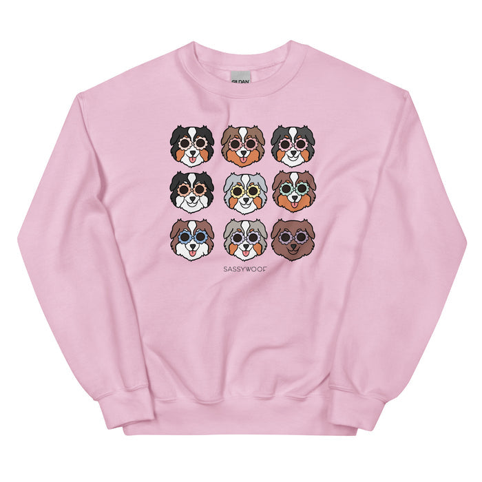 The Sassy Woof "Sweatshirt - Aussies" is a comfy pink unisex crewneck with nine cartoon Australian Shepherd faces in a grid and "SASSY WOOF" printed below.