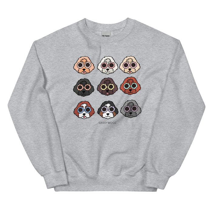 The Sweatshirt - Doodles by Sassy Woof is a comfy, gray unisex crewneck with a grid of nine cartoon dog faces in various fur colors and styles, plus “SASSY WOOF” text centered below.