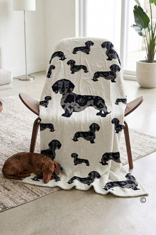 White blanket with black dachshund pattern draped over a chair in a room.