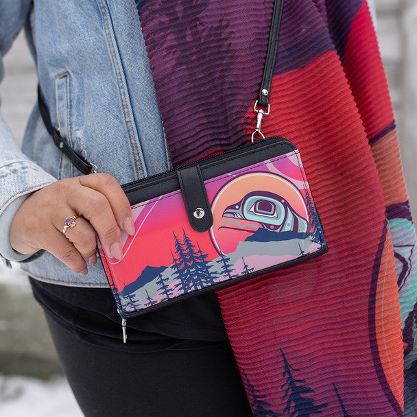 Person holding a colorful wallet with nature design, wearing a patterned jacket.