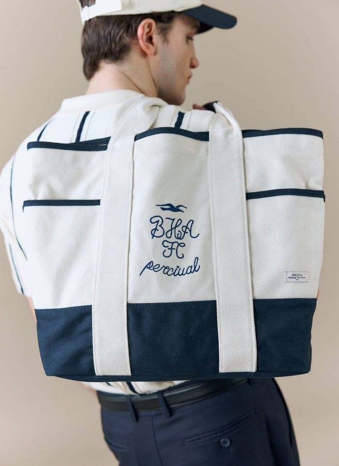 A model viewed from behind carries the Percival x Brighton & Hove Albion F.C. tote bag, showing the navy embroidery detail.