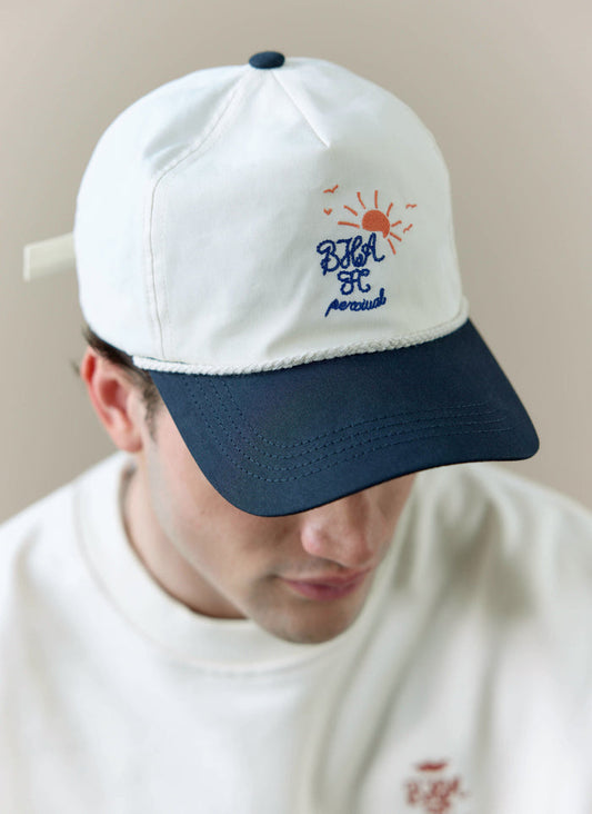 A close-up of a model wearing the cream and navy Trucker Cap from the Percival x Brighton & Hove Albion F.C. collaboration.