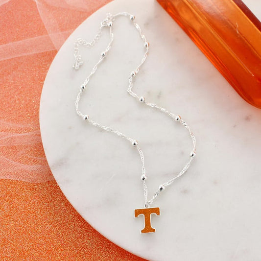 Silver necklace with a letter 'T' pendant on an orange and white background
