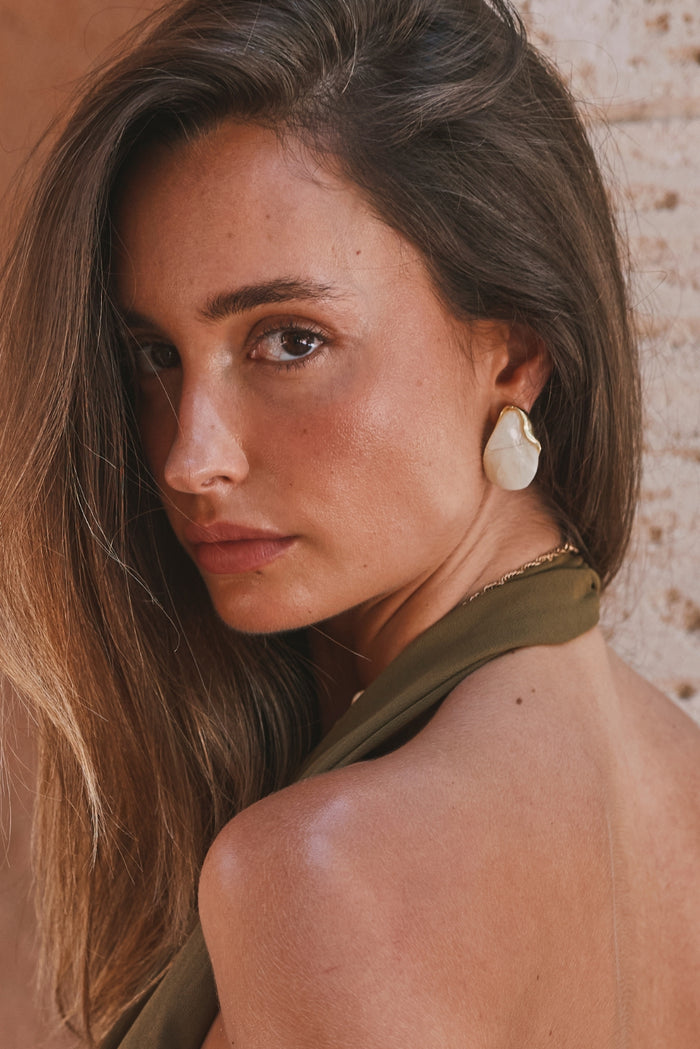 White Sands stone earring with gold trim worn against a sunlit stucco wall.