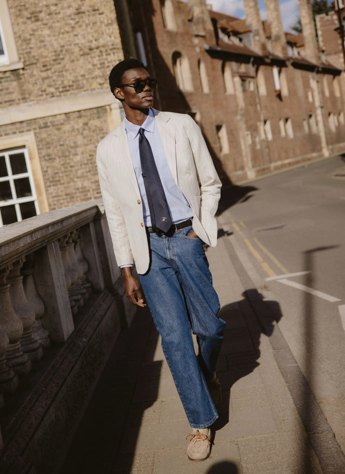 The navy silk World Key Tie from Percival, featuring a gold motif and styled on a model in a pinstripe blazer.